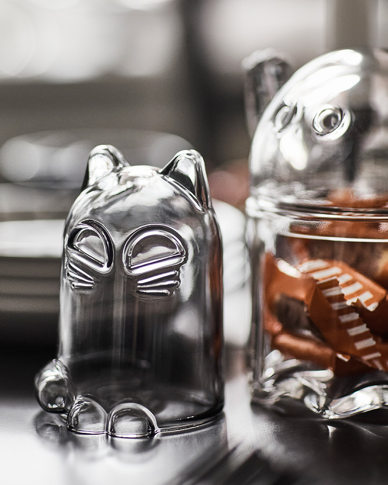 A KUSTFYR glass dome shaped like a cat is placed on a table next to a KUSTFYR bowl with lid shaped like a ghost.