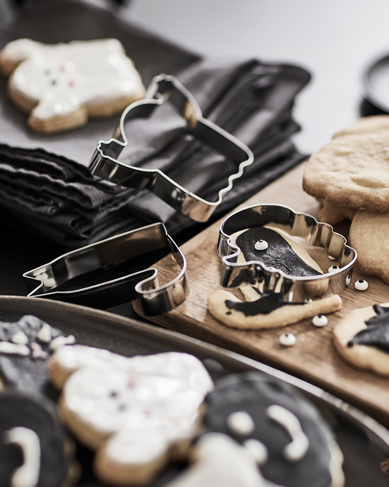Different KUSTFYR pastry cutters are placed on a black table alongside some Halloweenthemed decorated cookies.