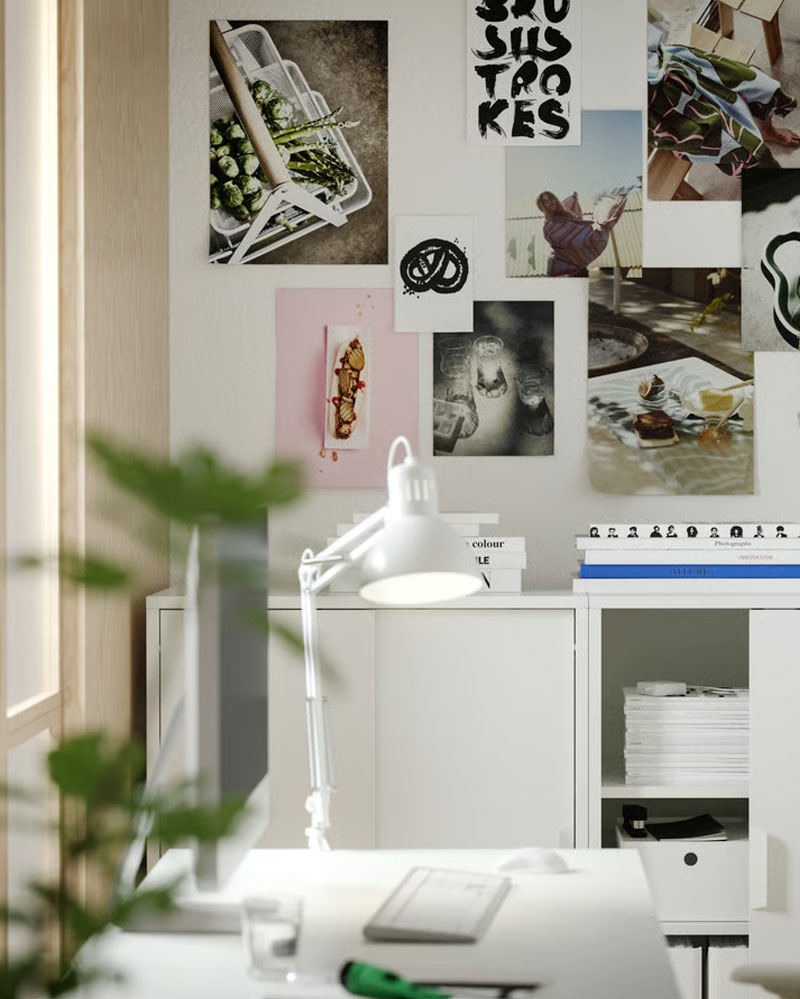 Two white TROTTEN cabinets with sliding doors, filled with magazines, standing side by side with a TROTTEN desk in the front.