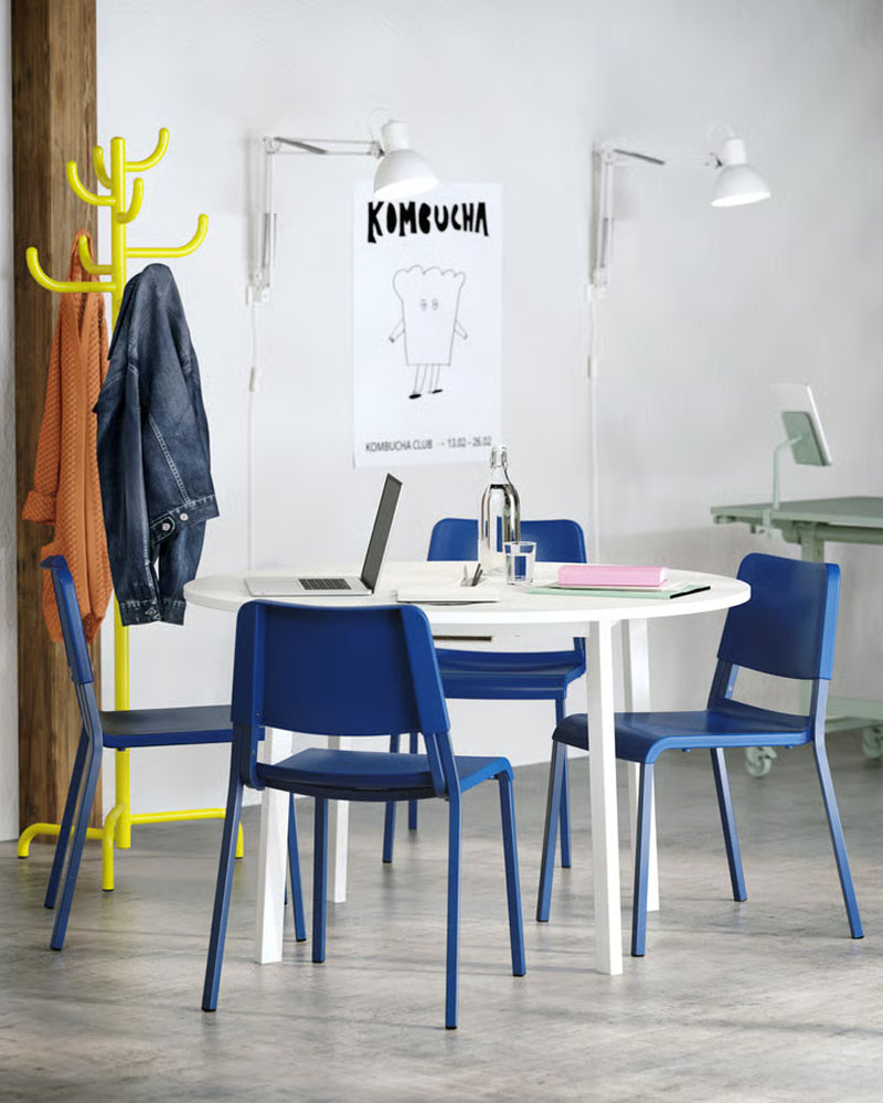 A white MITTZON conference table with four blue TEODORES chairs. A yellow steel hat and coat stand stands by the wall
