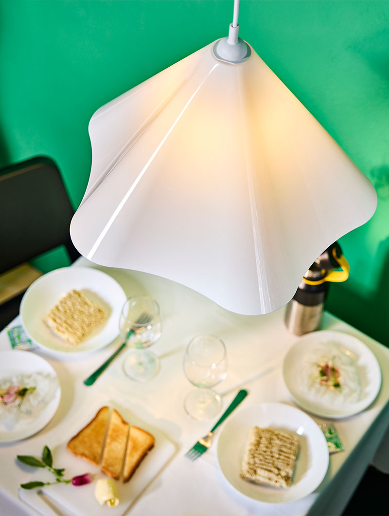 White plastic ZEBRASÄV pendant lamp hung over a dining table laid with white tablecloth and OFTAST dinnerware.