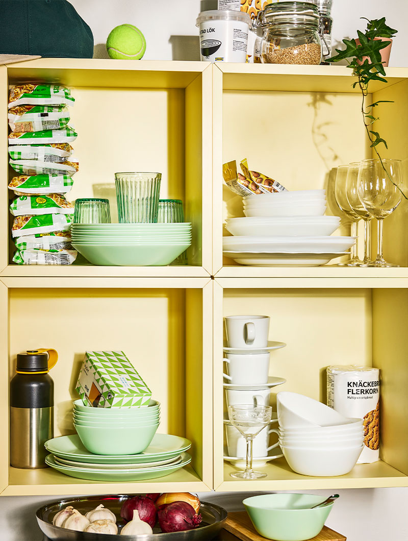 OFTAST dinnerware in light green and white on yellow shelves in student accommodation