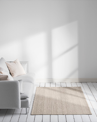 Alfombra de tejido natural en un salón minimalista con paredes blancas y suelo de madera clara, frente a un sofá de diseño simple con cojines suaves, realzado por la luz solar que proyecta sombras.