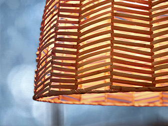 Detail of a woven bamboo pendant lamp shade with a herringbone pattern, showing how light filters through the openings creating a warm, textured effect.