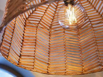 Close-up of a woven bamboo pendant lamp shade with a geometric pattern, revealing an illuminated vintage filament bulb inside.