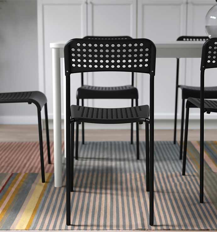 Black dining chairs with perforated seats and backs, arranged around a white table, placed on a rug with pastel colored stripes adding texture to the floor.