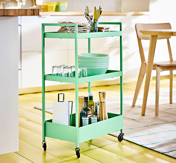 Carro verde con utensilios, vasos y botellas en cocina.