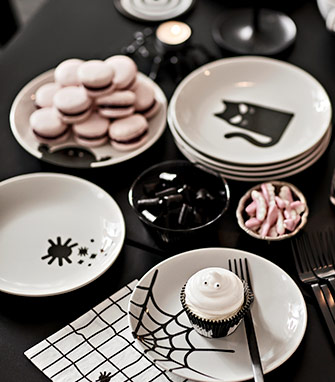 Mesa con platos de Halloween, dulces variados y cupcake fantasma.