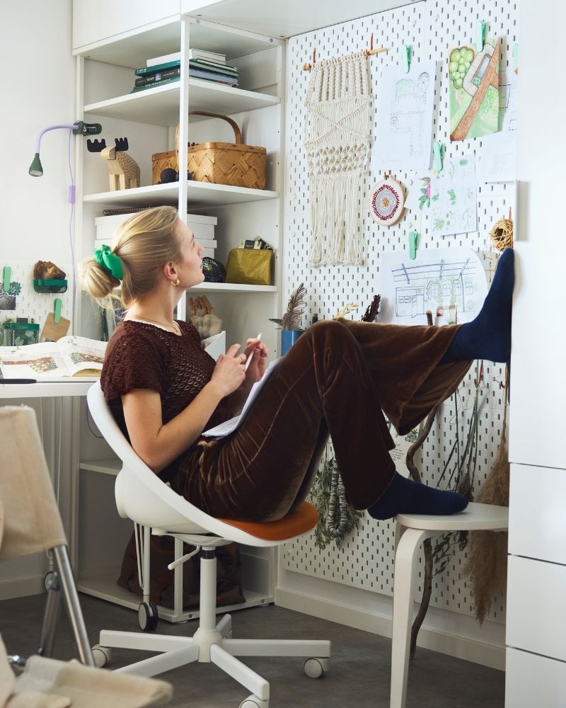A person in a desk chair looking at a wall with SKÅDIS pegboards used with accessories holding sketches and study essentials.