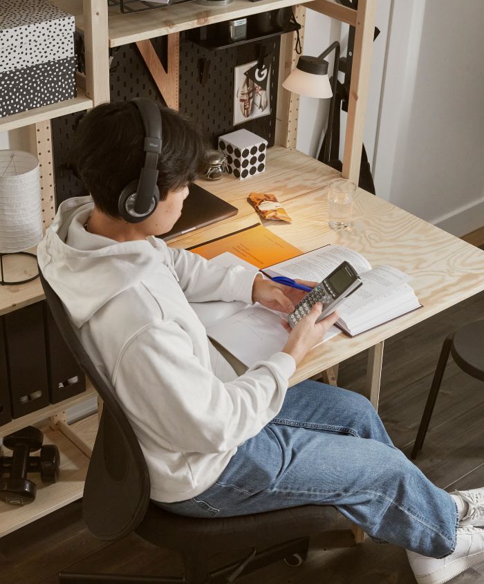 A teenager studying by an IVAR folding table in pine attached to an IVAR shelving unit holding black and white objects.