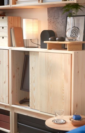 Two IVAR cabinets in pine with sliding doors displaying decorative objects and a lamp on top, placed next to a side table.