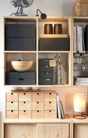 Two IVAR wall shelves in pine holding black storage boxes and other objects, placed above IVAR cabinets with sliding doors.