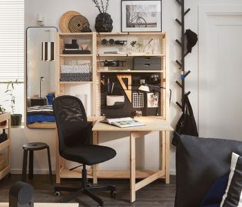 An IVAR folding table used as a desk attached to IVAR shelving unit, all in pine, used with a black desk chair.