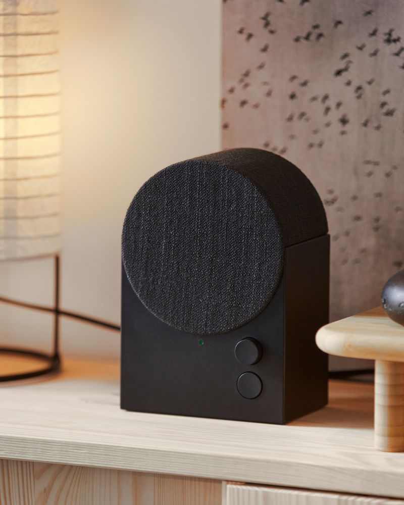 The black NATTBAD Bluetooth speaker with a rounded shape and two buttons on the front is standing on top of a pine cabinet.