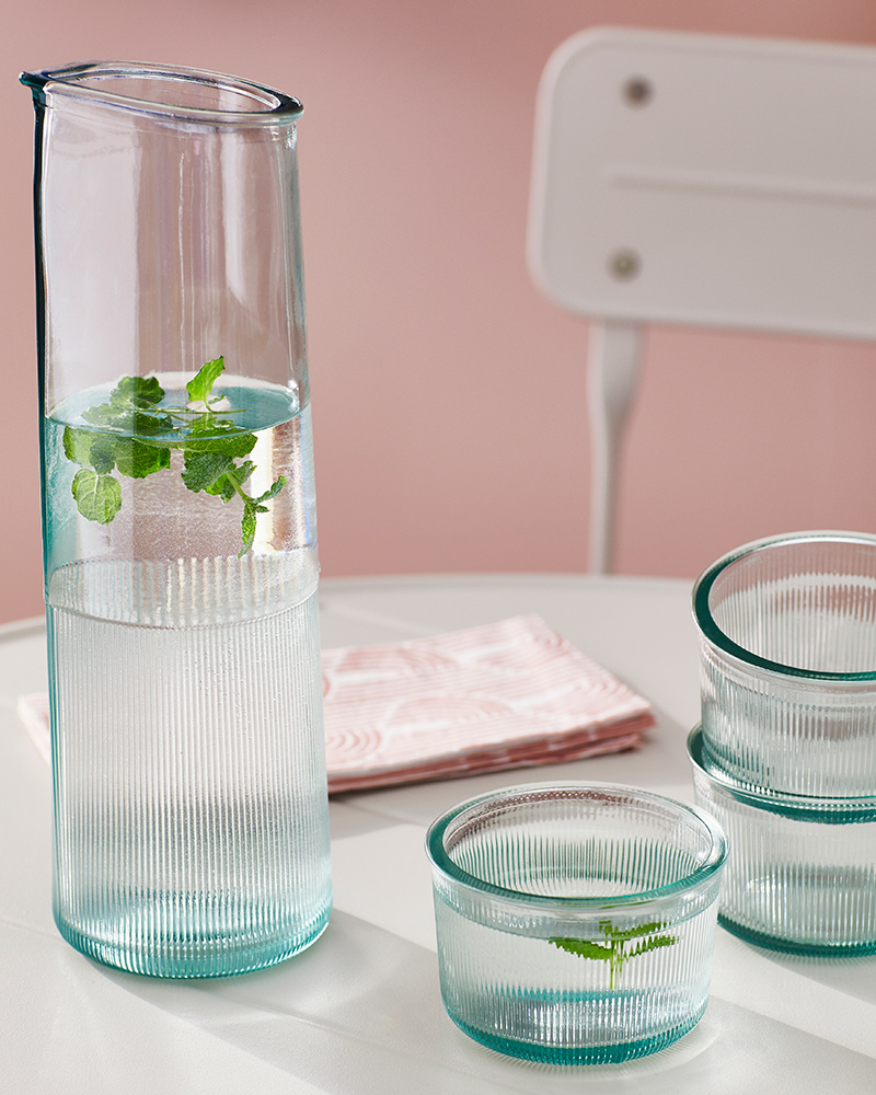 A BERGVATTNET carafe, glasses, and a napkin are placed on an off-white SUNDSÖ table with a folding chair next to it.