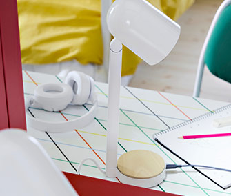 Lámpara de mesa blanca con base de madera sobre escritorio estampado. Auriculares y libreta, esenciales para tu estudio.