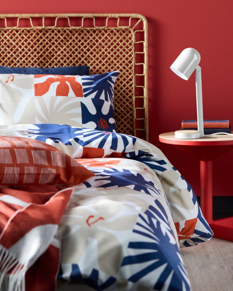 Un dormitorio rojo con una cama con cabecero tejido y ropa de cama con estampado de hojas azules, naranjas y blancas.