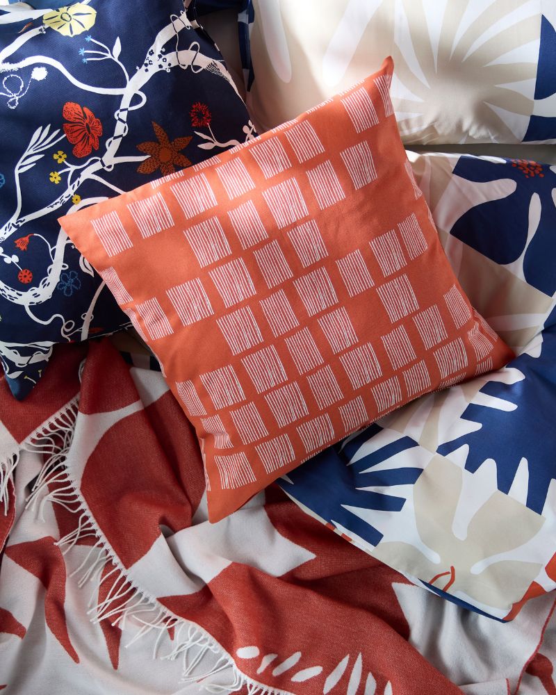 Primer plano de una pila de almohadas y una manta con varios patrones, incluidos diseños florales en naranja, azul y rojo.