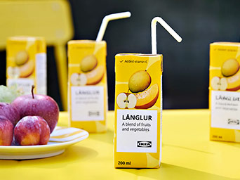 LÅNGLUR juice boxes from IKEA with apple and melon flavor, ready to drink. Red apples are on the yellow table.