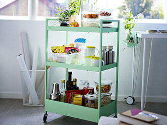 Carrito de metal verde claro con tres estantes. Lleno de comida y utensilios de cocina. Práctico para cualquier espacio del hogar