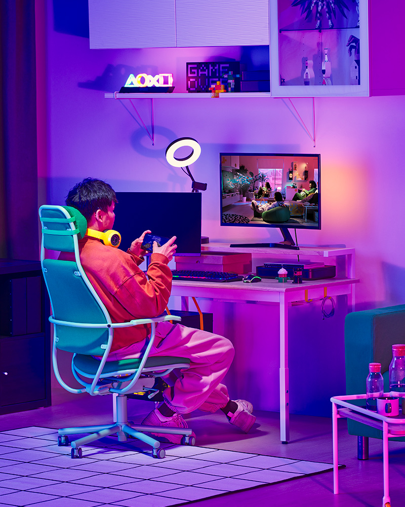 Un joven jugando videojuegos en una silla gamer LÖPARBANA frente a su computadora, y a la derecha, una mesa auxiliar BRÄNNBOLL.