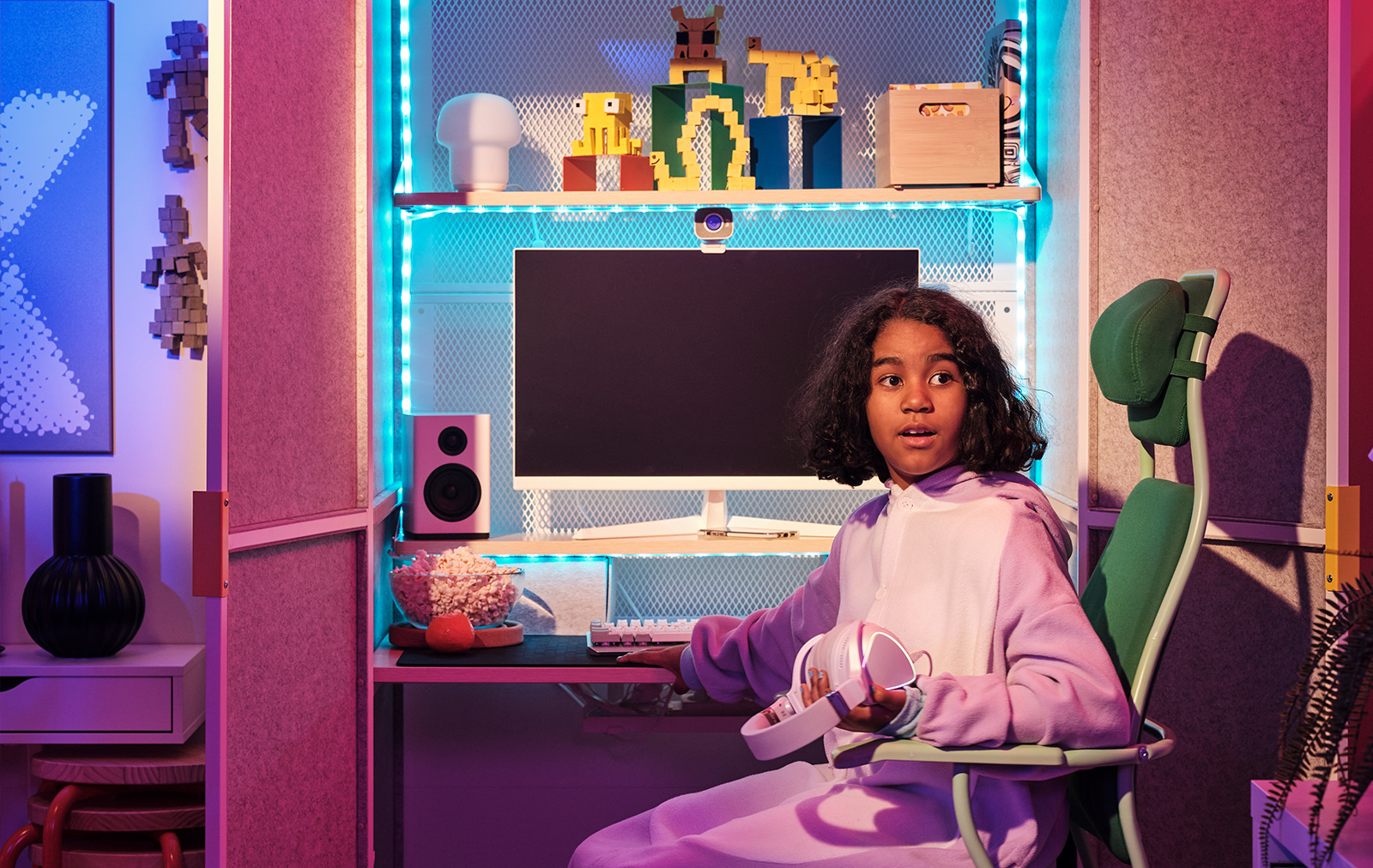 Niña con pijama rosa sentada en una silla verde LÖPARBANA frente a una estación de juego BRÄNNBOLL.