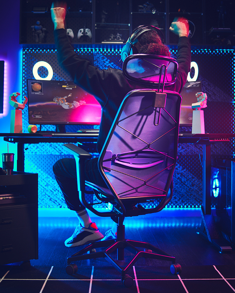 Niño sentado en un conjunto de silla y escritorio gamer UTESPELARE/STYRSPEL, disfrutando de una sesión de juego con un soporte para auriculares LÅNESPELARE a su derecha.