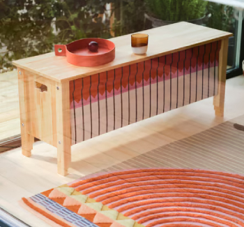 Banco de madera hecho a mano con frente en colores otoñales, bandeja de color rojo intenso, vaso rústico y alfombra artesanal a juego en tonos cálidos.