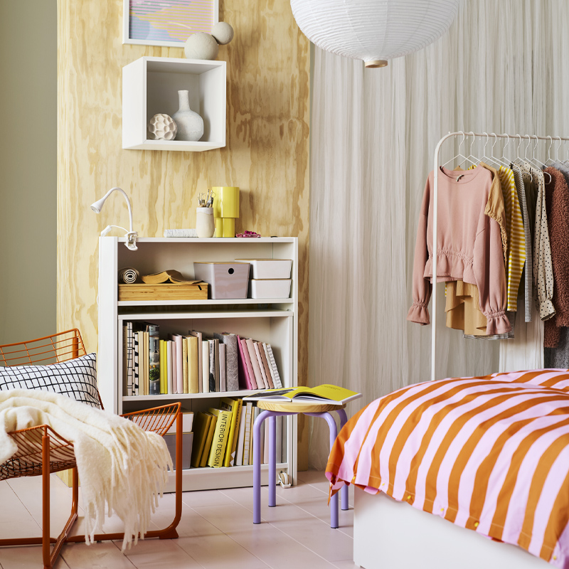 Una estantería BILLY blanca con mesa plegable contra una pared de madera clara con un foco LED NÄVLINGE con pinza en el estante superior.