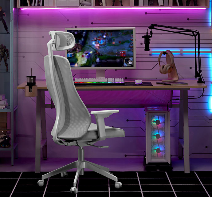 Silla ergonómica de escritorio gris frente a una mesa de gaming con pantalla, teclado y micrófono. Luces LED en la pared.