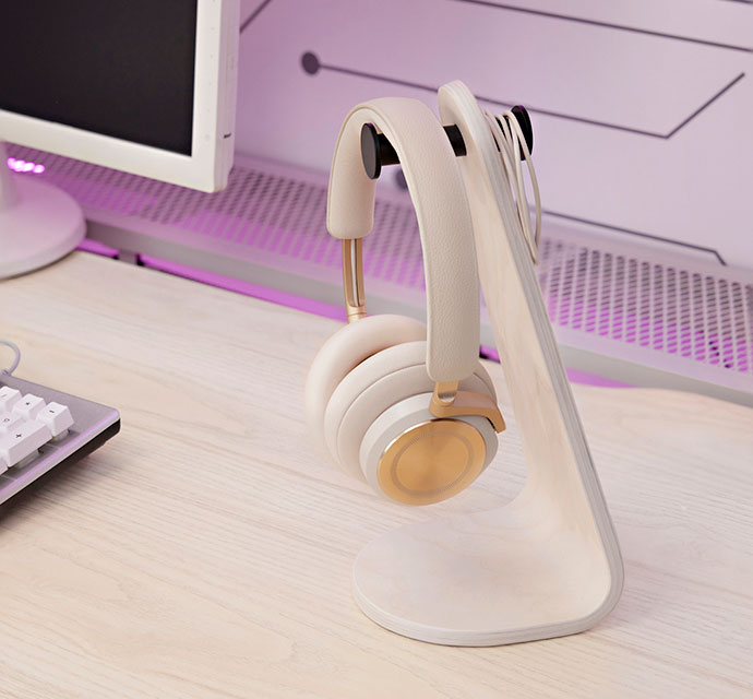 Primer plano de unos auriculares de diadema beige y dorados, colgados en un soporte de madera clara.