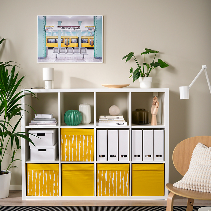 Shelving unit with yellow abstract-patterned storage boxes and white binders. Colorful and organized storage solution for home offices.