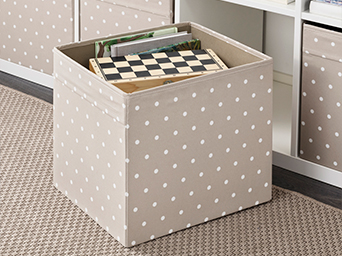 Storage box in beige with white polka dots, holding a chess set and books. Decorative solution for shelves, ideal for living rooms.