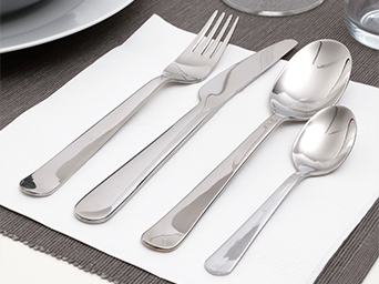 Un juego de cubiertos de acero inoxidable, con un tenedor, un cuchillo, una cuchara y una cucharilla. Están sobre una servilleta blanca y un mantel individual gris.