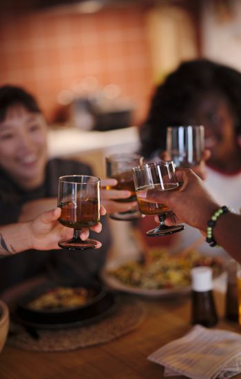 Four people at a table, each holding an IKEA 365+ goblet fi lled with drinks, reaching towards one another for a toast. 