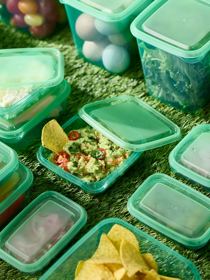 Varios recipientes alimentarios ecológicos PRUTA con tapas sobre una mesa. Uno de los recipientes está abierto y lleno de comida, con la tapa apoyada sobre él.