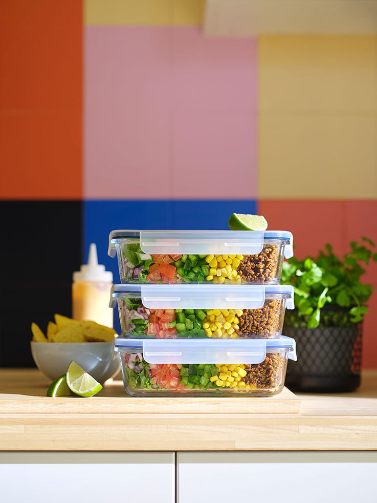 Tres recipientes para alimentos IKEA 365+ con tapa, apilados uno encima del otro, que contienen alimentos, y un bol IKEA 365+ con patatas fritas.