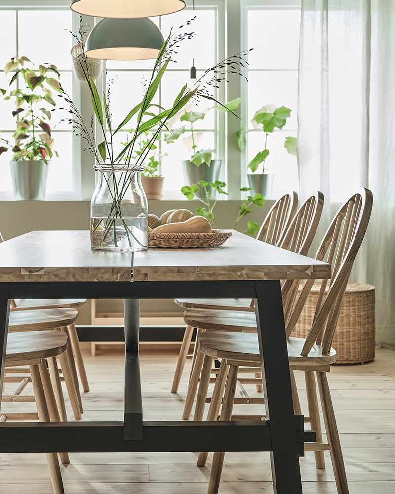 Una mesa SKOGSTA con un jarrón BEGÄRLIG encima y varias sillas SKOGSTA, iluminadas por dos lámparas colgantes RÖDFLIK en el comedor.