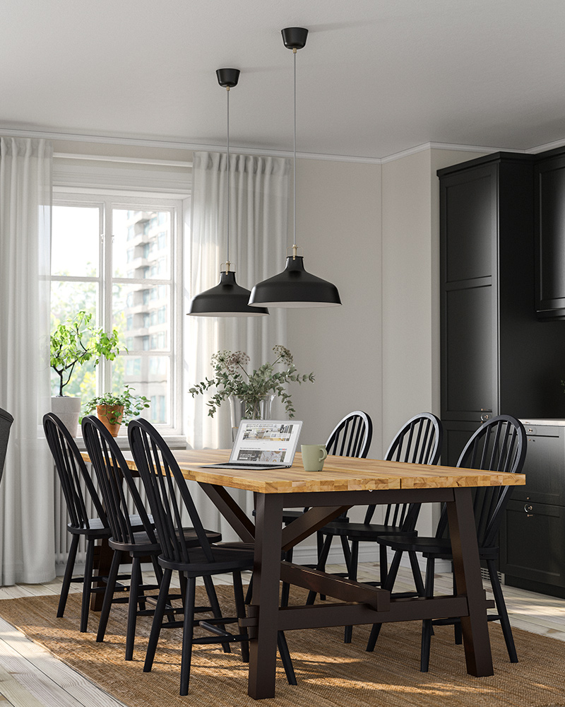 Una mesa SKOGSTA y varias sillas SKOGSTA negras, iluminadas por dos lámparas colgantes RANARP en el comedor.