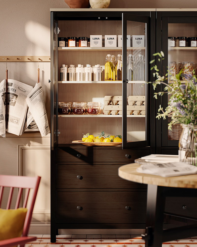 Frascos y botellas están exhibidos en una vitrina HEMNES de color negro-marrón con puertas de vidrio y tres cajones, en una recepción de estilo clásico.