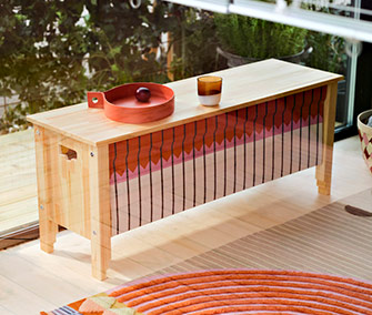 Banco de madera con un panel de tela estampada y una bandeja roja en la parte superior.