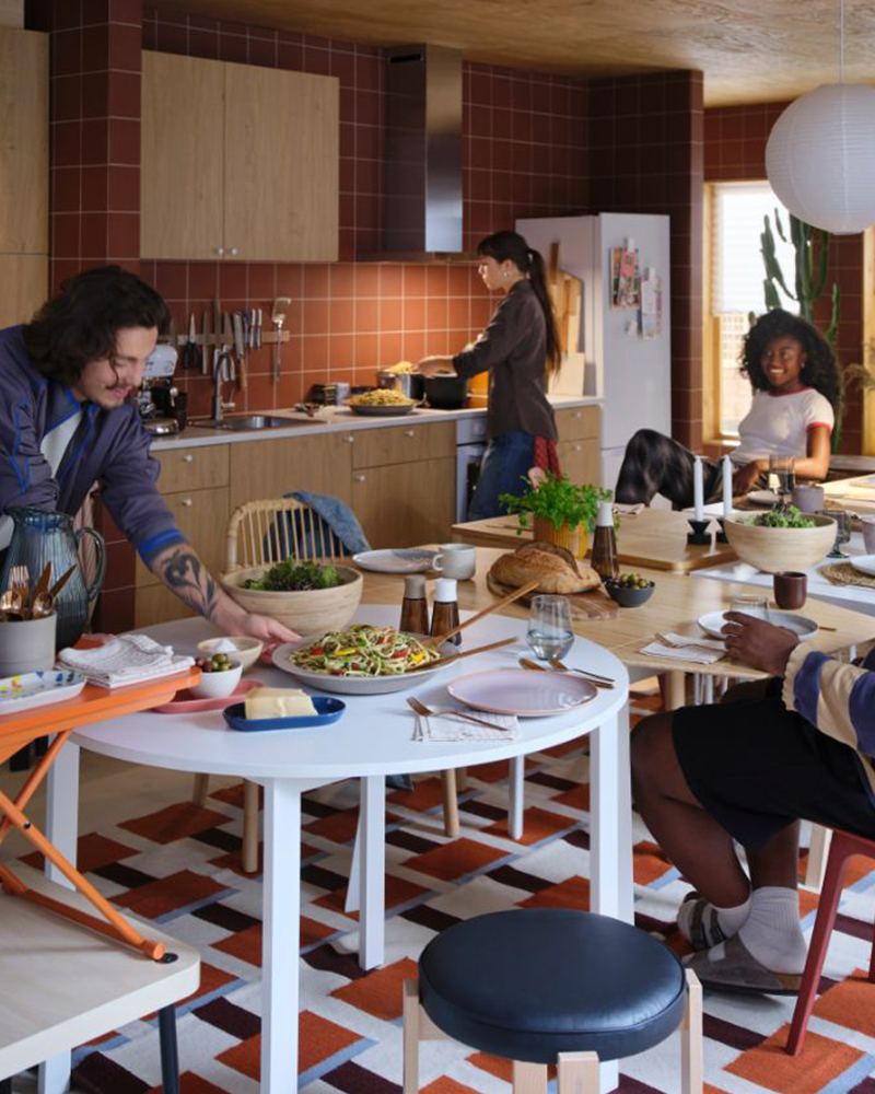 Four people are preparing for a meal in a lively kitchen. One of them is placing food on a set, white VIHALS table. 