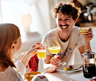 Smiling couple toasting with glasses of orange juice at a breakfast table.
