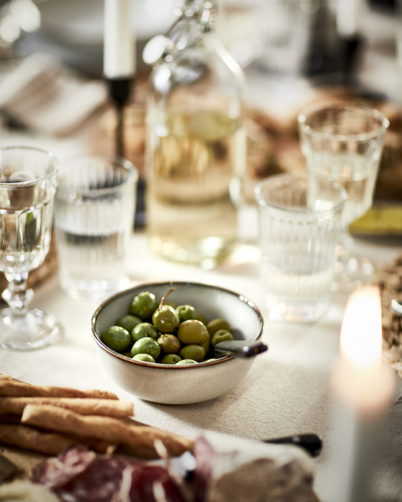 Cuenco con aceitunas verdes sobre mesa acogedora con copas, botella y velas.