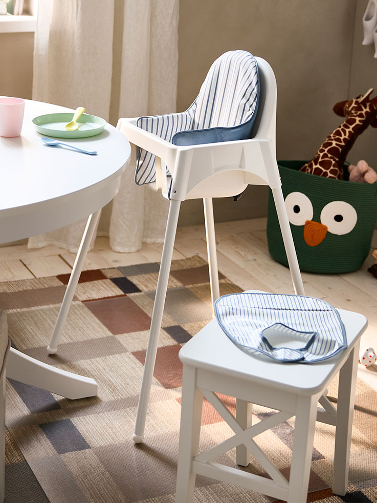 A white ROSENTORP stool and an ANTILOP highchair with tray are standing next to a white ROSENTORP extendable table.