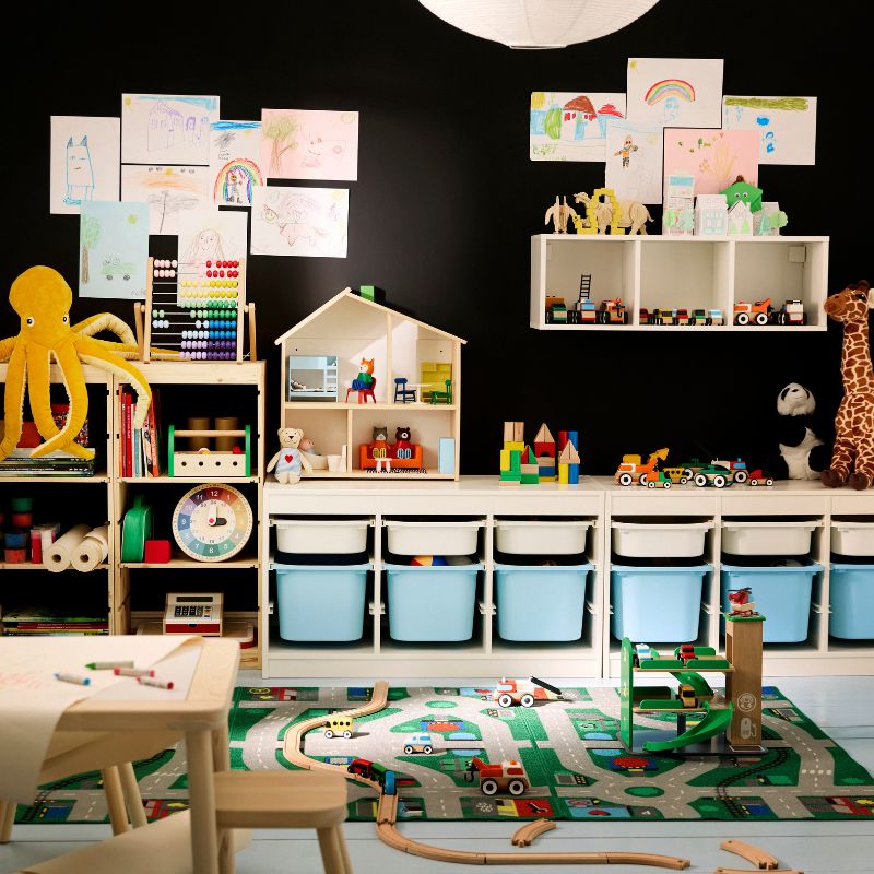 Cuarto de juegos infantil colorido con paredes negras, un escritorio de madera clara y almacenamiento. Contenedores azules y blancos.