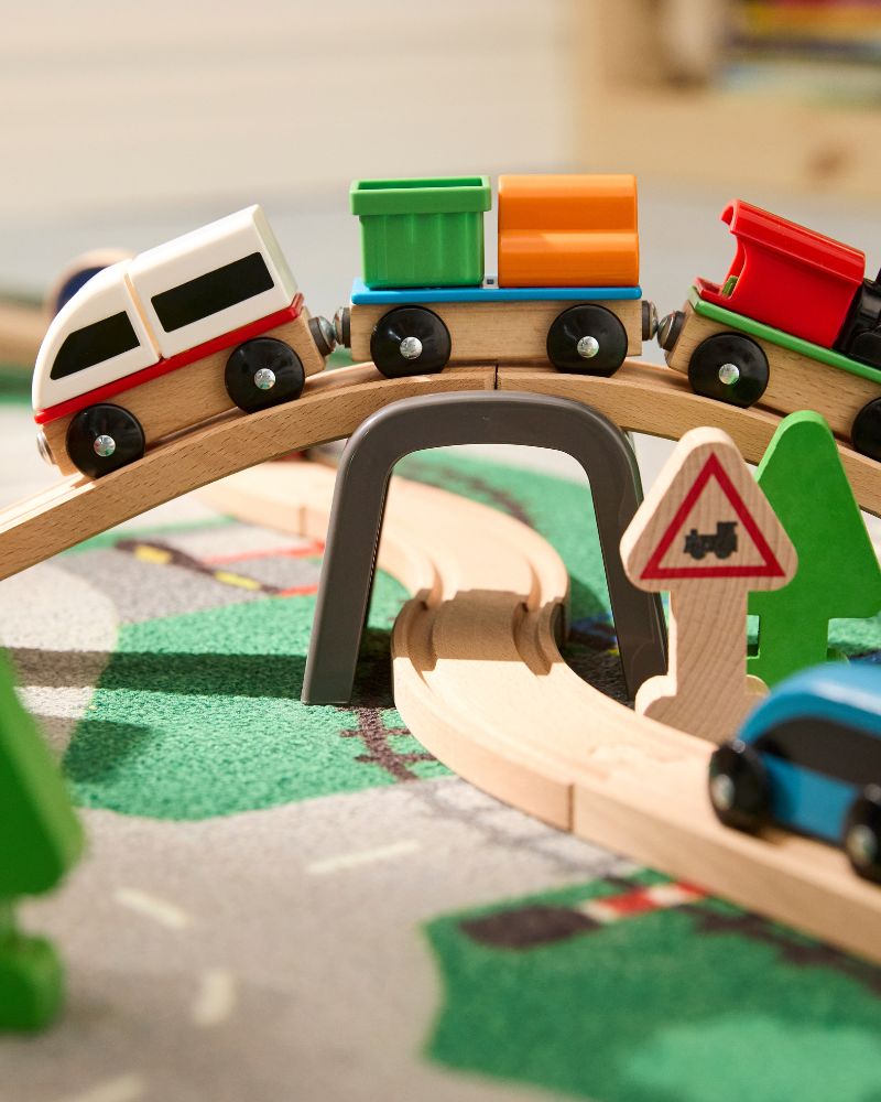 Un tren de juguete rojo, blanco, verde y naranja en una vía y un puente de madera.
