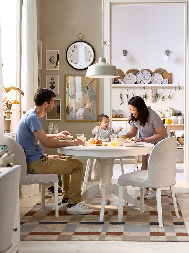 A dining area has a white ROSENTORP extendable table and two chairs, with a view of a kitchen area in the background
