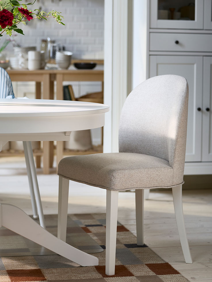 A fully-upholstered ROSENTORP chair in Kilanda light beige/white is placed next to a white ROSENTORP extendable table.