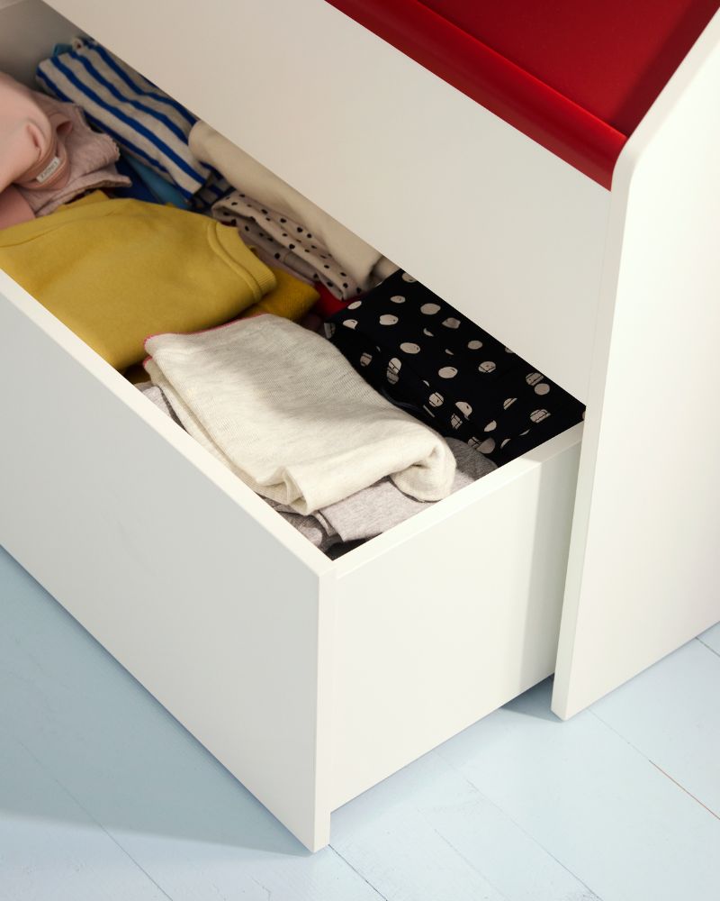 Primer plano de un cajón blanco lleno de ropa de colores, incluyendo prendas amarillas y a rayas.